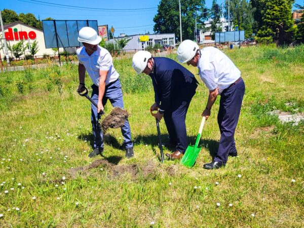 Trzech mężczyzn w białych kaskach, kopiących szpadlami w na działce budowlanej.