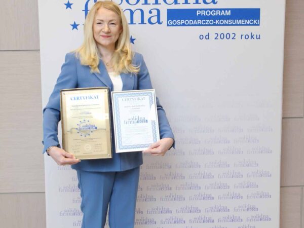 na zdjęciu kobieta trzymająca w dłoniach certyfikaty na tle ścianki z napisem solidna firma