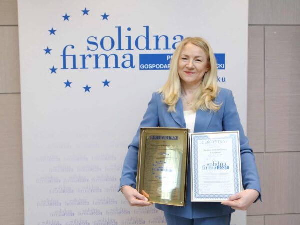 na zdjęciu kobieta trzymająca w dłoniach certyfikaty na tle ścianki z napisem solidna firma